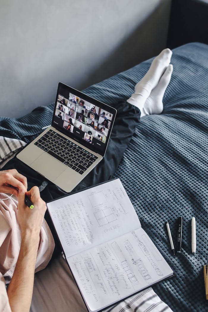 Person engaging in a video call while studying on a laptop at home.